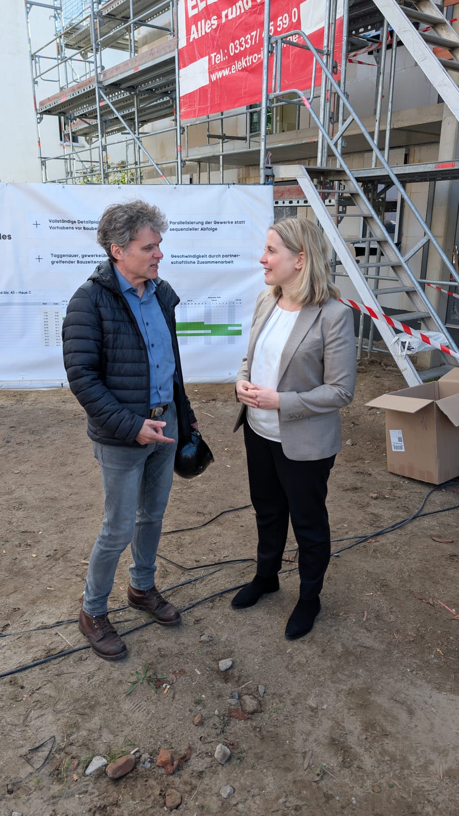 Ronald Meyer im Gespräch mit Bundesbauministerin Verena Hubertz vor dem Bauzeitenplan an der Baustelle